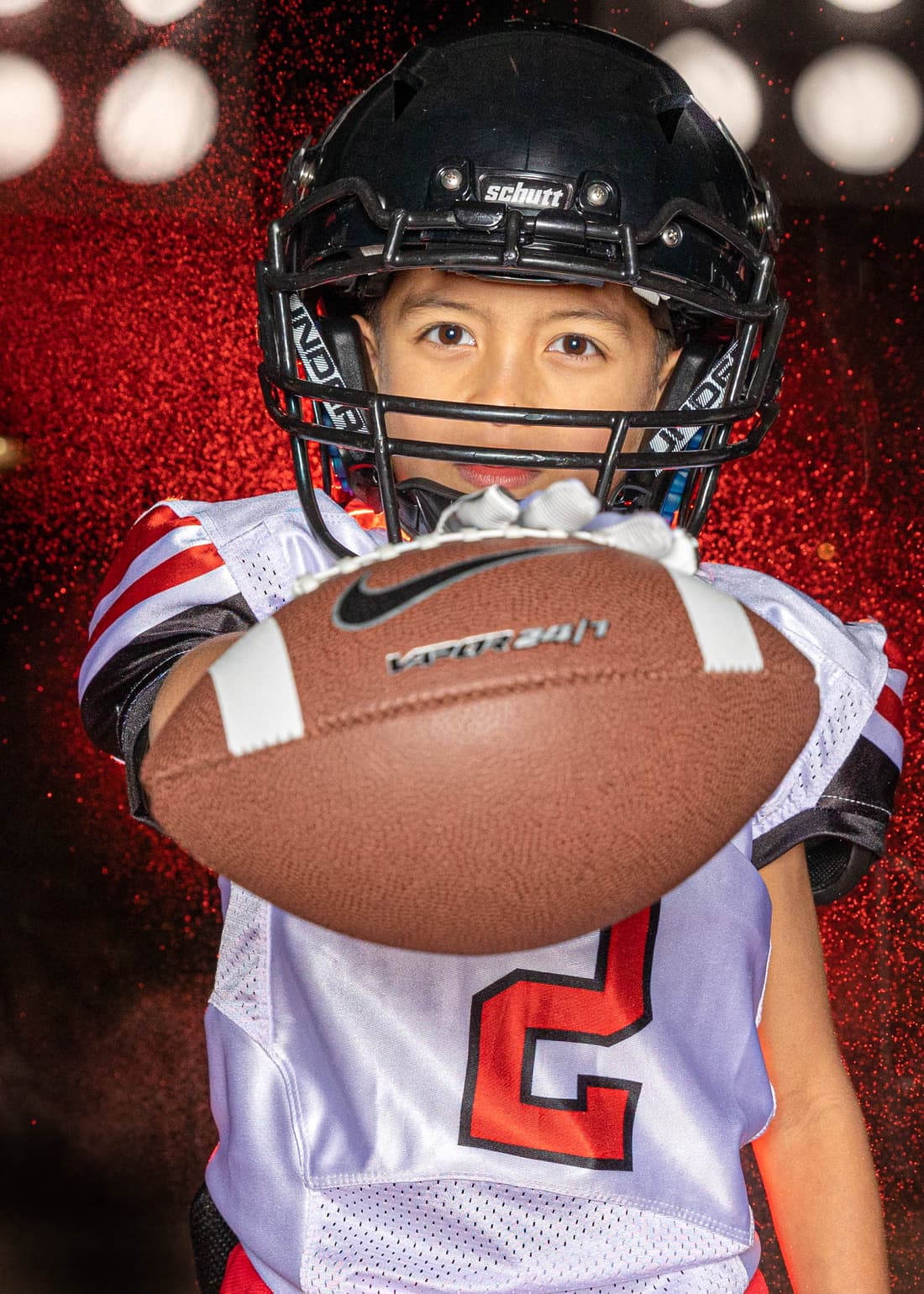 Young football player in full pads against a red sparkle backdrop