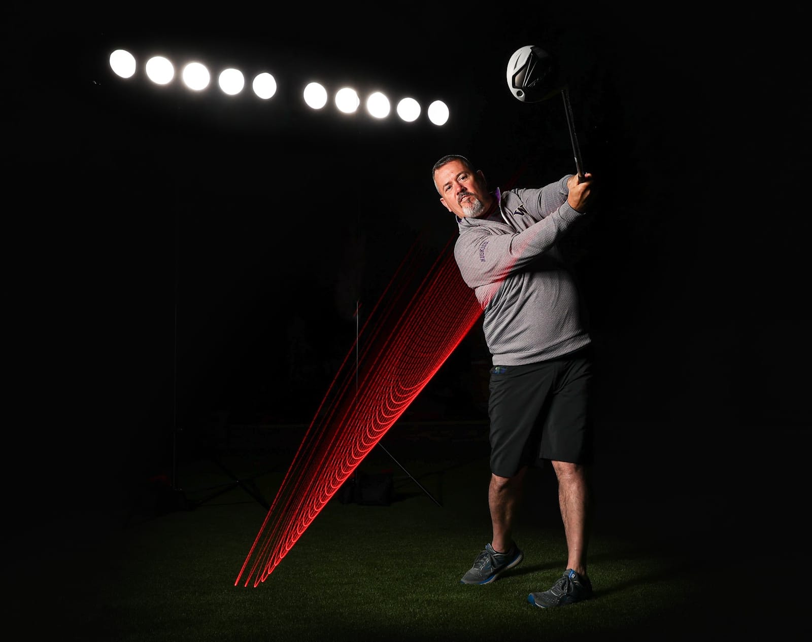 Golf swing traced in red light against a dark studio