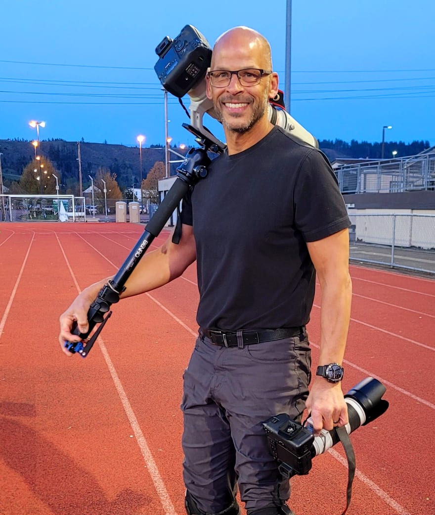 Tim Mackey of STK Photography at the track at dusk, carrying three cameras