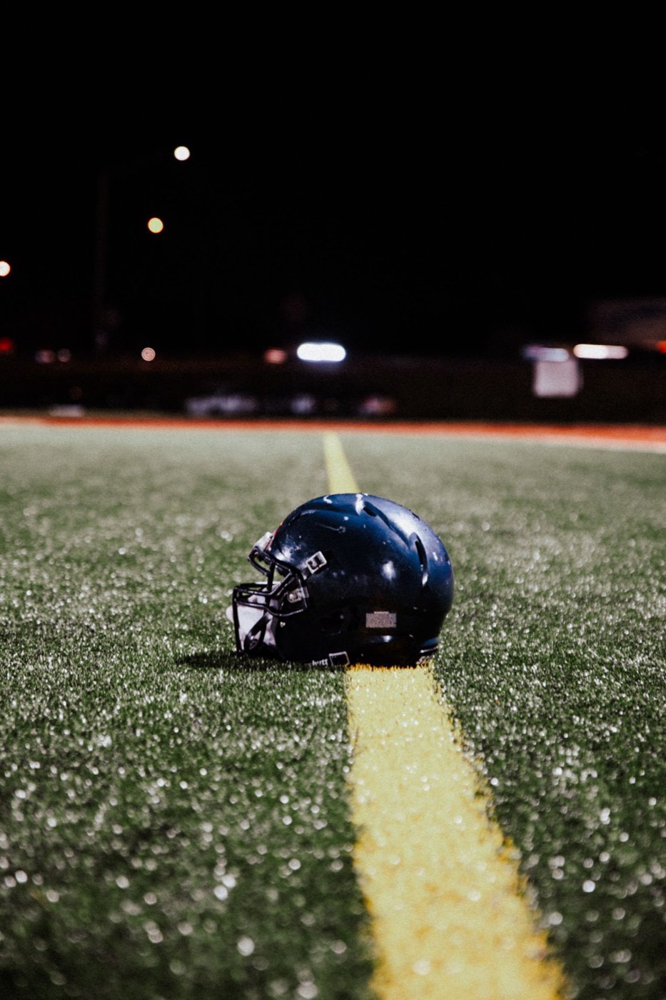 A lone football helmet left on the field under the lights